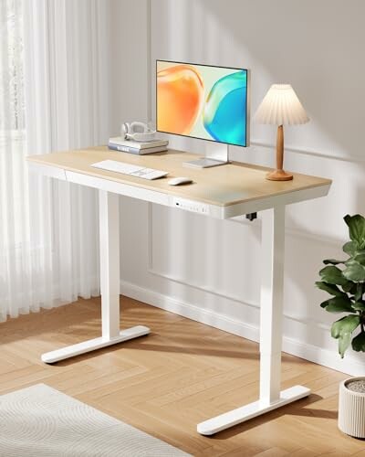 Modern standing desk with monitor, keyboard, lamp, and plant.